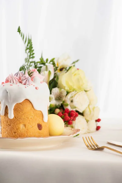 Foco seletivo de delicioso bolo de Páscoa decorado com merengue com ovos rosa e branco na placa perto de flores e talheres — Fotografia de Stock