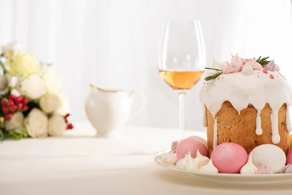 Foco seletivo de delicioso bolo de Páscoa decorado com merengue com ovos rosa e branco na placa perto de copo de vinho e flores — Fotografia de Stock