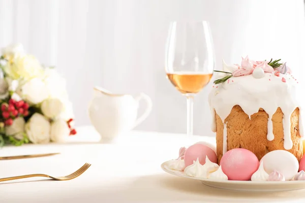 Foco seletivo de delicioso bolo de Páscoa decorado com merengue com ovos rosa e branco na placa perto de copo de vinho e flores — Fotografia de Stock