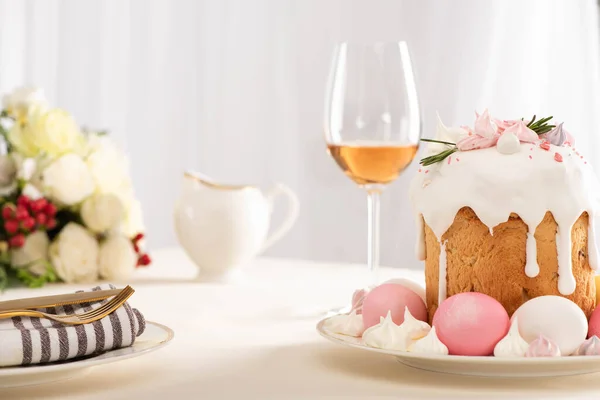 Selective focus of delicious Easter cake decorated with meringue with pink and white eggs on plate near wine glass and flowers — Stock Photo