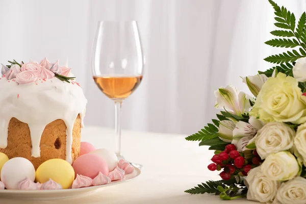 Délicieux gâteau de Pâques décoré de meringue aux œufs roses et blancs sur assiette près des fleurs et du vin — Photo de stock