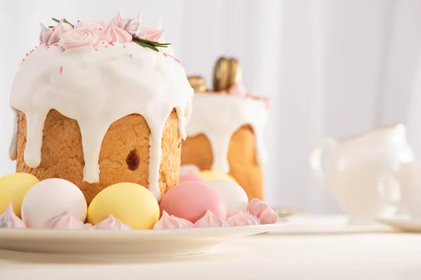 Selective focus of delicious Easter cakes decorated with meringue near colorful eggs on plates — Stock Photo