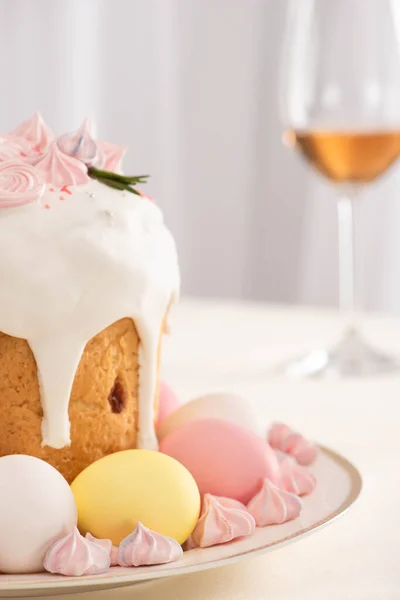 Foco selectivo de pastel de Pascua decorado con merengue cerca de huevos de colores en el plato y copa de vino - foto de stock