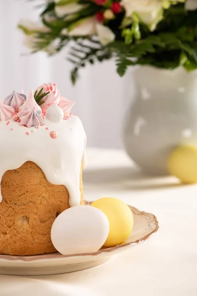 Messa a fuoco selettiva di deliziosa torta di Pasqua decorata con meringa vicino uova colorate sul piatto sul tavolo con vaso di fiori — Foto stock