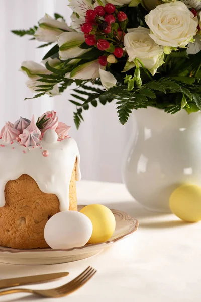 Köstliche Ostertorte mit Baiser in der Nähe von bunten Eiern auf Teller auf Tisch mit Blumenvase und Besteck dekoriert — Stockfoto