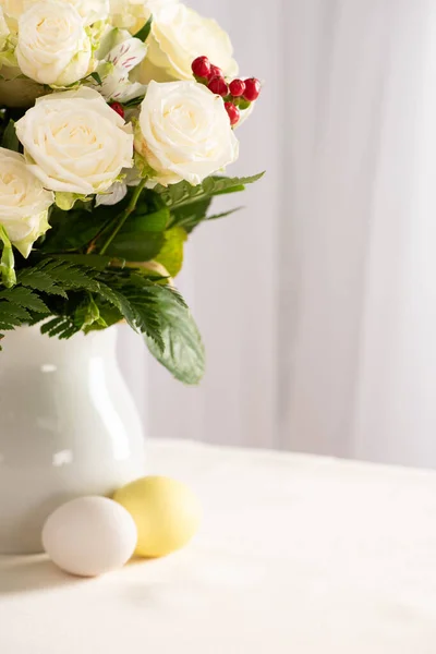 Vase of fresh flowers on table near colorful Easter eggs — Stock Photo