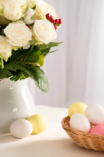 Vase of fresh flowers on table near colorful Easter eggs in basket — Stock Photo