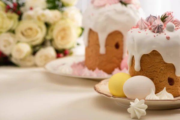 Messa a fuoco selettiva di deliziose torte pasquali decorate con meringa vicino alle uova su piatto e fiori — Foto stock