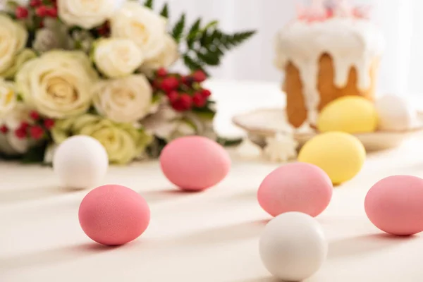Селективный фокус окрашенных яиц вблизи вкусного пасхального торта и цветов — стоковое фото