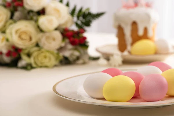 Enfoque selectivo de huevos pintados en el plato cerca de deliciosa tarta de Pascua y flores - foto de stock
