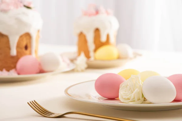 Selective focus of delicious Easter cakes with meringue near colorful eggs on plate and fork — Stock Photo