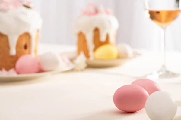 Selective focus of delicious Easter cakes with meringue and colorful eggs on plates near wine glass — Stock Photo