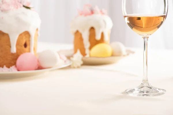 Enfoque selectivo de deliciosos pasteles de Pascua con merengue y huevos de colores en platos cerca de la copa de vino - foto de stock