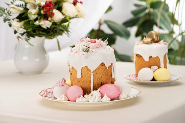 Selective focus of Easter cakes with colorful eggs near flowers in vase on table — Stock Photo