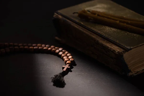 Enfoque selectivo de la Biblia santa con velas y rosario con cruz en la oscuridad con la luz del sol - foto de stock