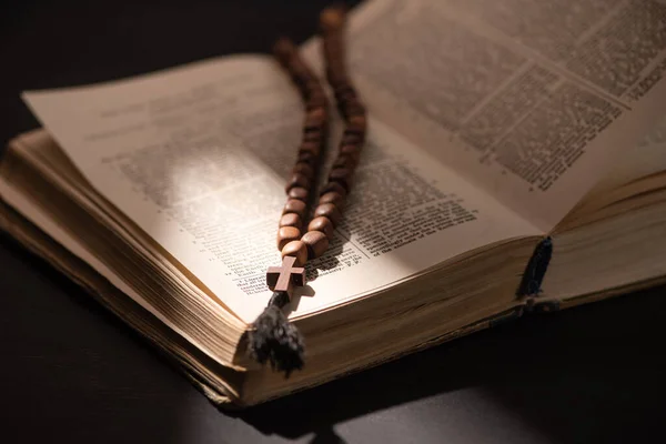 KYIV, UKRAINE - JANUARY 17, 2020: open holy bible and rosary with cross in dark with sunlight — Stock Photo