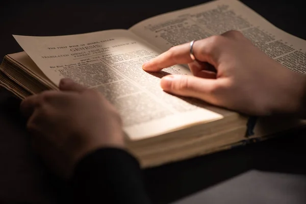 KYIV, UCRANIA - 17 DE ENERO DE 2020: vista recortada de la mujer leyendo la sagrada Biblia en la oscuridad con la luz del sol - foto de stock