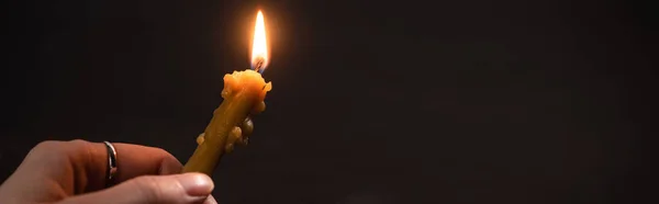 Cropped view of woman holding burning church candle in dark, panoramic shot — Stock Photo