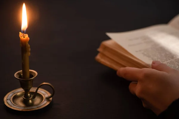 Ausgeschnittene Ansicht einer Frau mit heiliger Bibel in der Nähe brennender Kerze im Dunkeln — Stockfoto