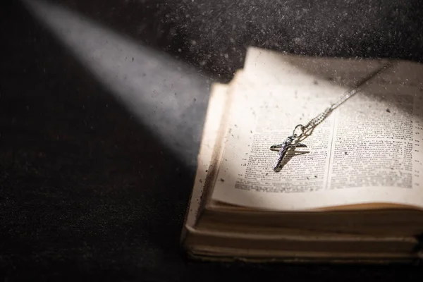 KYIV, UKRAINE - 17 JANVIER 2020 : bible sainte ouverte avec croix catholique et cendres dans l'obscurité avec la lumière du soleil — Photo de stock