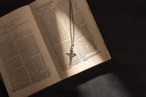 KYIV, UKRAINE - JANUARY 17, 2020: top view of open holy bible with cross on dark background with sunlight — Stock Photo