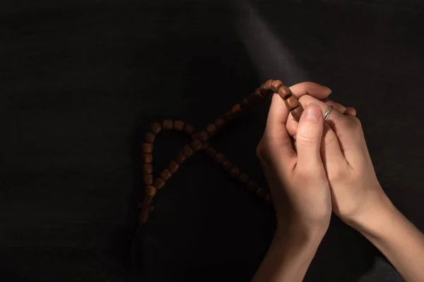 Cropped view of woman praying with rosary on dark background — Stock Photo