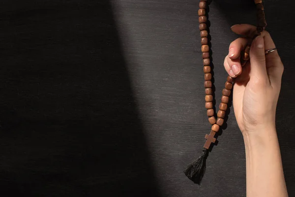 Cropped view of woman praying with rosary on dark background — Stock Photo