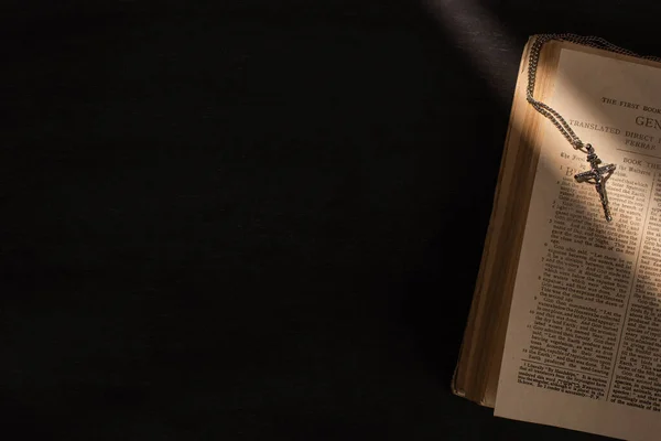 KYIV, UKRAINE - JANUARY 17, 2020: top view of open holy bible with cross on dark background with sunlight — Stock Photo