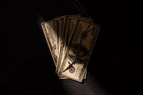 Vista superior del dinero y cruz sobre fondo oscuro con luz solar - foto de stock