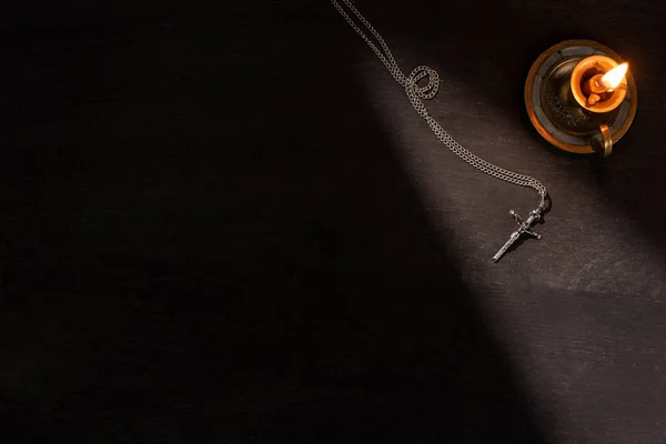 Top view of burning candle and cross on dark background with sunlight — Stock Photo