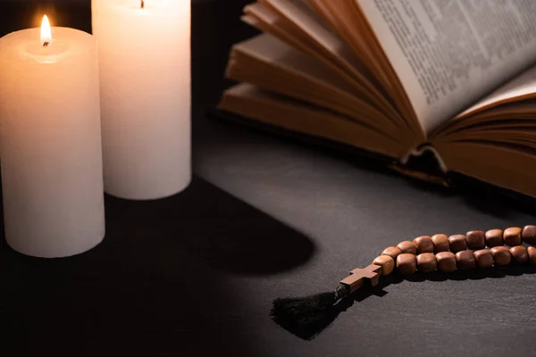 Sainte Bible avec chapelet sur fond noir foncé avec des bougies allumées — Photo de stock