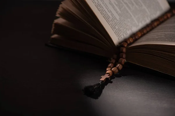 Sainte Bible avec chapelet sur fond noir foncé avec lumière du soleil — Photo de stock