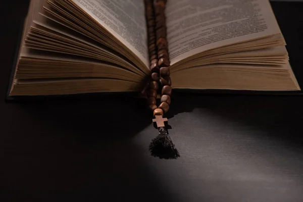 Sainte Bible avec chapelet sur fond noir foncé avec lumière du soleil — Photo de stock