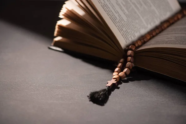 Священна Біблія з розарієм на чорному темному фоні з сонячним світлом — стокове фото