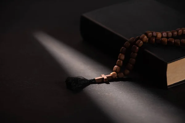 Sainte Bible avec chapelet sur fond noir foncé avec lumière du soleil — Photo de stock