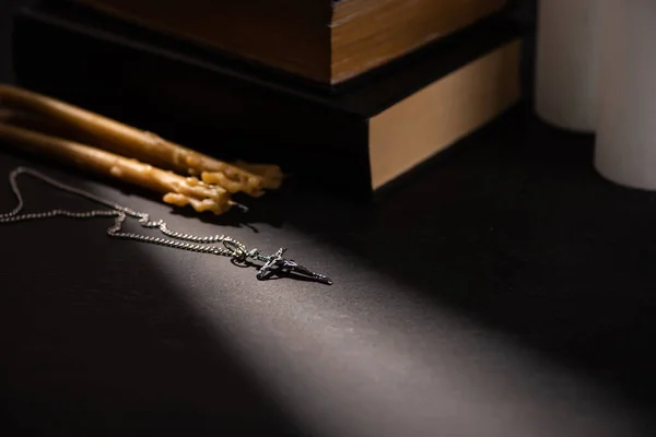 Croix et bougies d'église près de la bible sainte sur fond noir sombre avec la lumière du soleil — Photo de stock