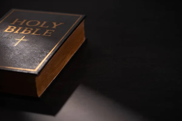 Biblia santa sobre fondo negro oscuro con luz solar - foto de stock