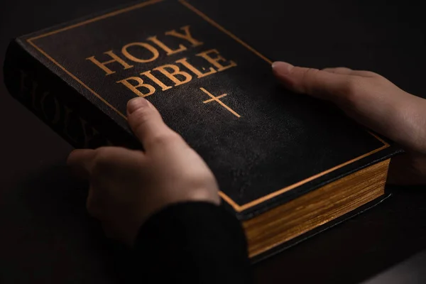 Cropped view of woman holding holy bible in dark — Stock Photo