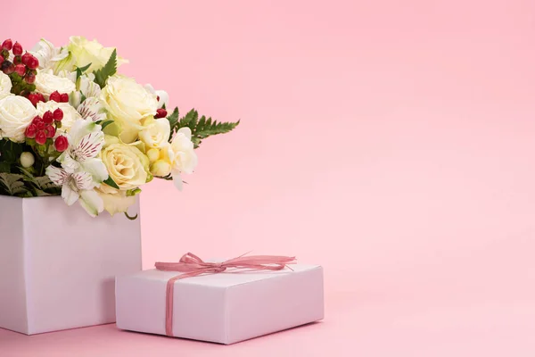 Bouquet of flowers in festive gift box with bow on pink background — Stock Photo