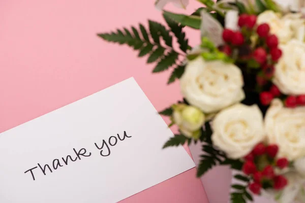Foco selectivo de ramo de flores en la caja de regalo festiva cerca gracias tarjeta de felicitación sobre fondo rosa - foto de stock