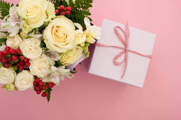 Vue du haut du bouquet de fleurs et boîte cadeau festive avec arc sur fond rose — Photo de stock