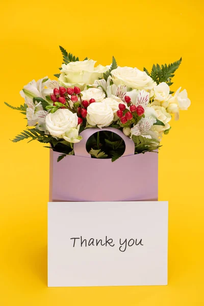 Primavera ramo fresco de flores en bolsa de papel violeta cerca de la tarjeta de agradecimiento aislado en amarillo - foto de stock