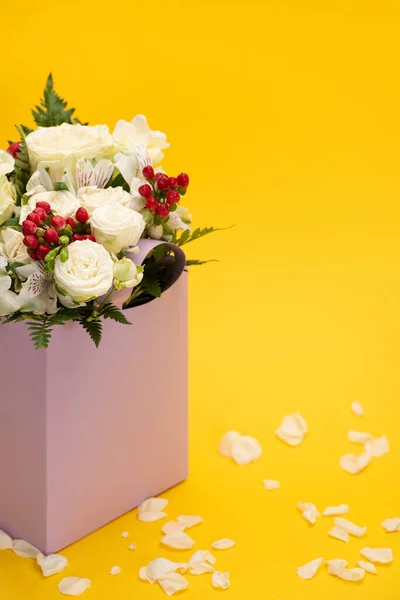 Primavera ramo fresco de flores en bolsa de papel violeta cerca de pétalos dispersos aislados en amarillo - foto de stock