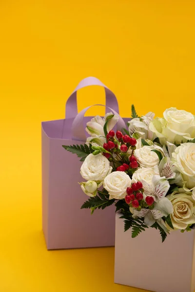 Bouquet de fleurs fraîches printanières dans une boîte cadeau festive près d'un sac en papier sur fond jaune — Photo de stock
