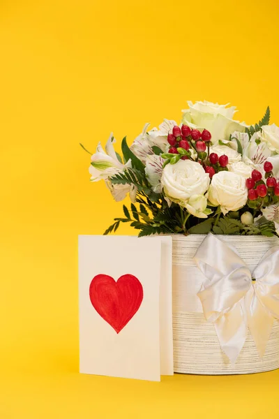 Spring fresh bouquet of flowers in festive gift box with bow near valentines card on yellow — Stock Photo