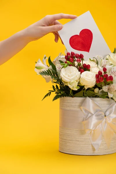 Vista ritagliata della donna mettendo biglietto di San Valentino in primavera bouquet fresco di fiori in scatola regalo festivo con fiocco sul giallo — Foto stock