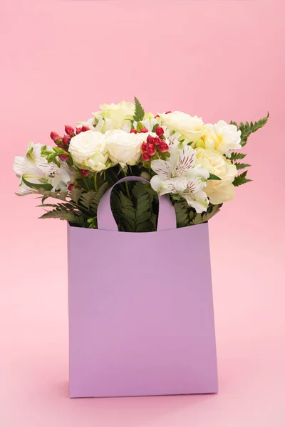 Bouquet of flowers in violet paper bag on pink background — Stock Photo