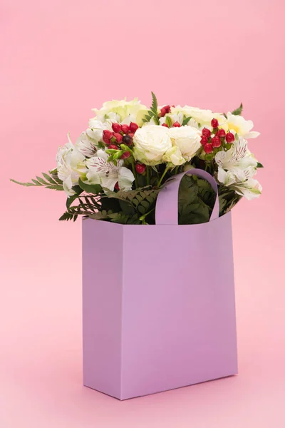 Bouquet of flowers in violet paper bag on pink background — Stock Photo