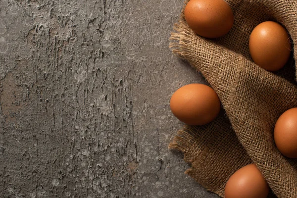 Вид зверху на коричневі яйця на мішковині на сірому текстурованому фоні — стокове фото
