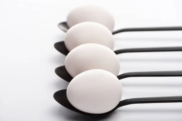 Selective focus of white chicken eggs on black spoons on white background — Stock Photo